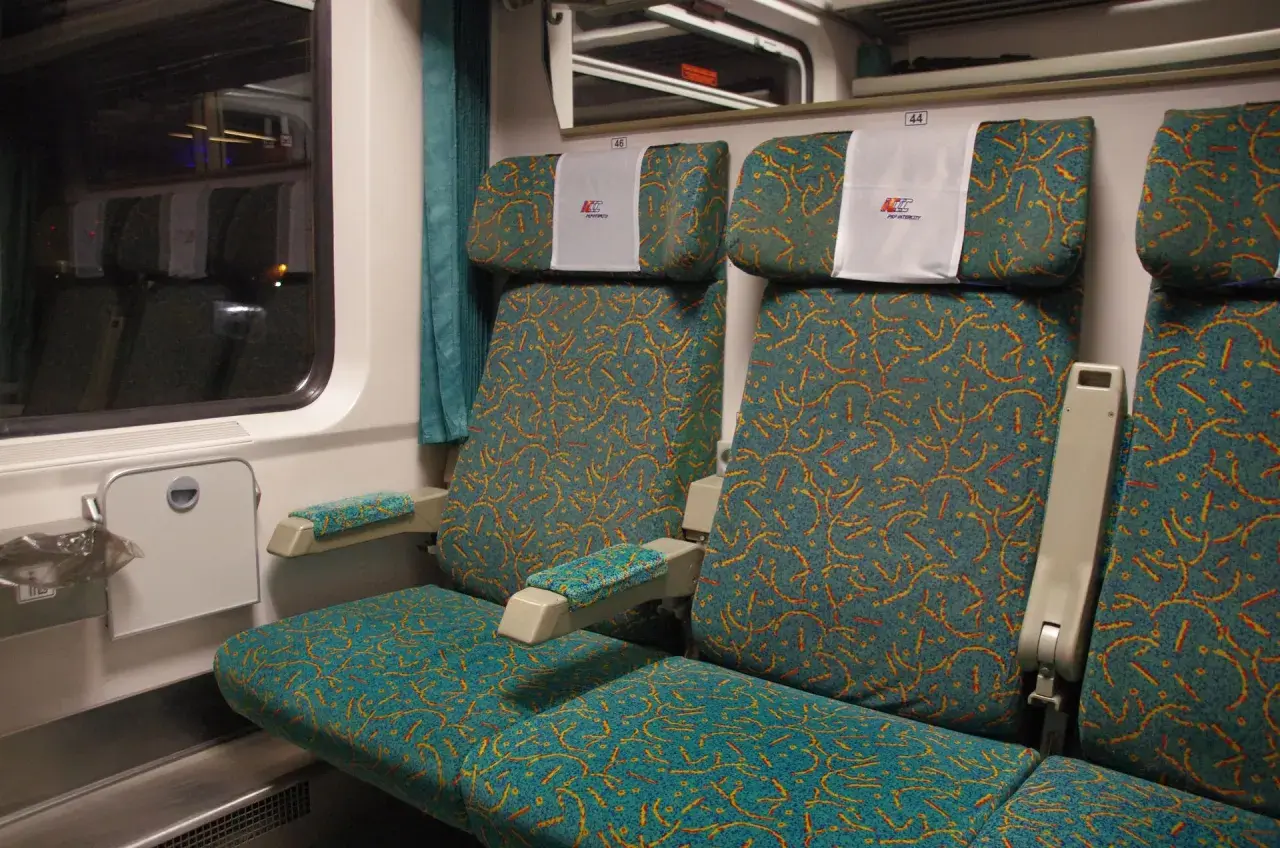 Wnętrze wagonu PKP Intercity. Widok na dwa rzędy siedzeń z charakterystycznym wzorem. Wybór miejsca ze schematu jest kluczowy dla komfortowej podróży.