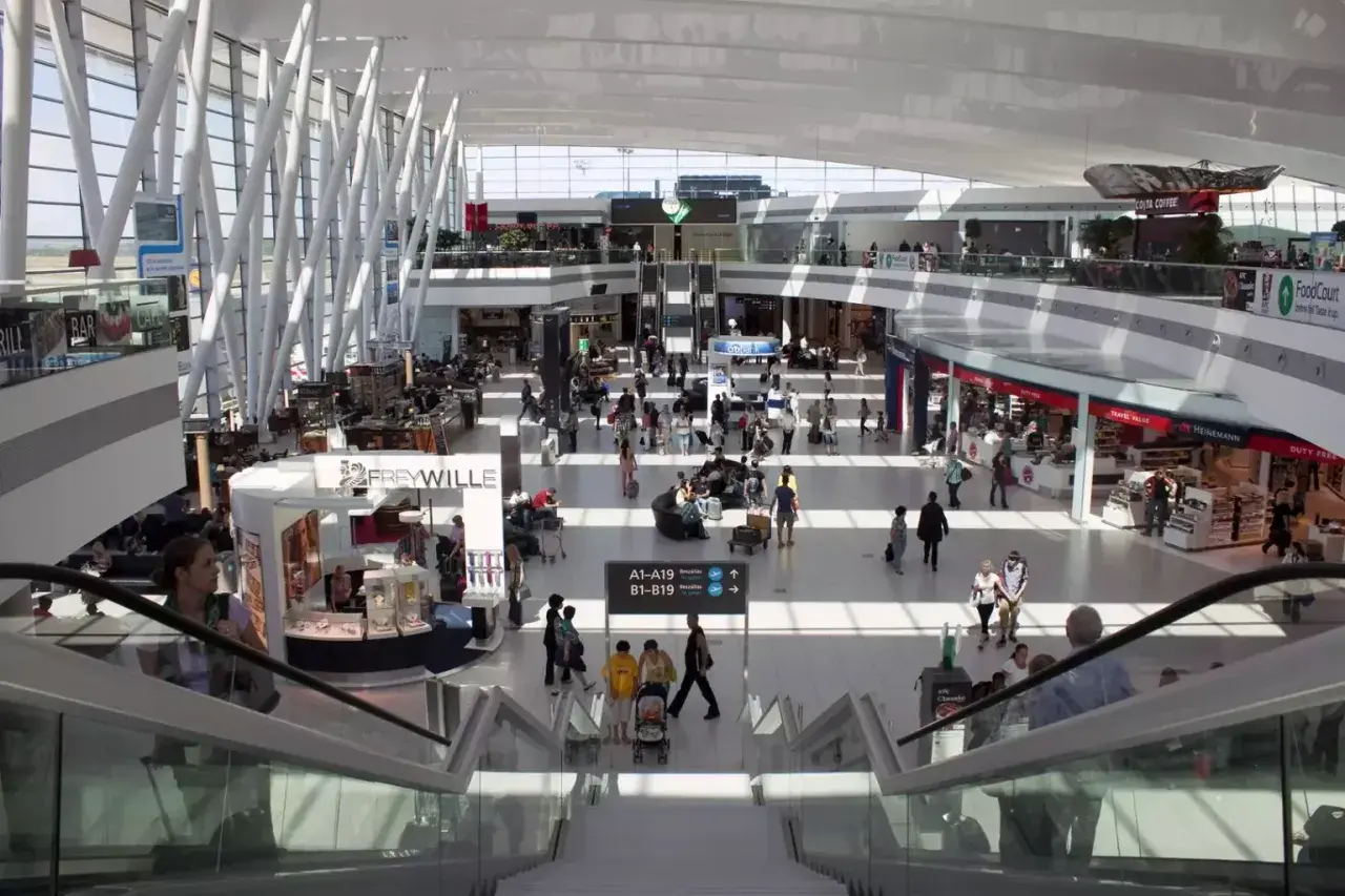 Tętniący życiem terminal lotniska w Budapeszcie. Ludzie poruszają się po nowoczesnej przestrzeni, szukając transportu z lotniska, sklepów i kawiarni.