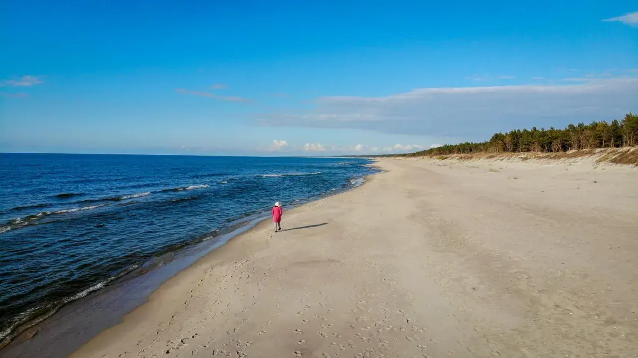 Samotna postać w różowym płaszczu spaceruje po plaży w Krynicy Morskiej. Wyobraź sobie, że to ostatni wagon pociągu do raju.