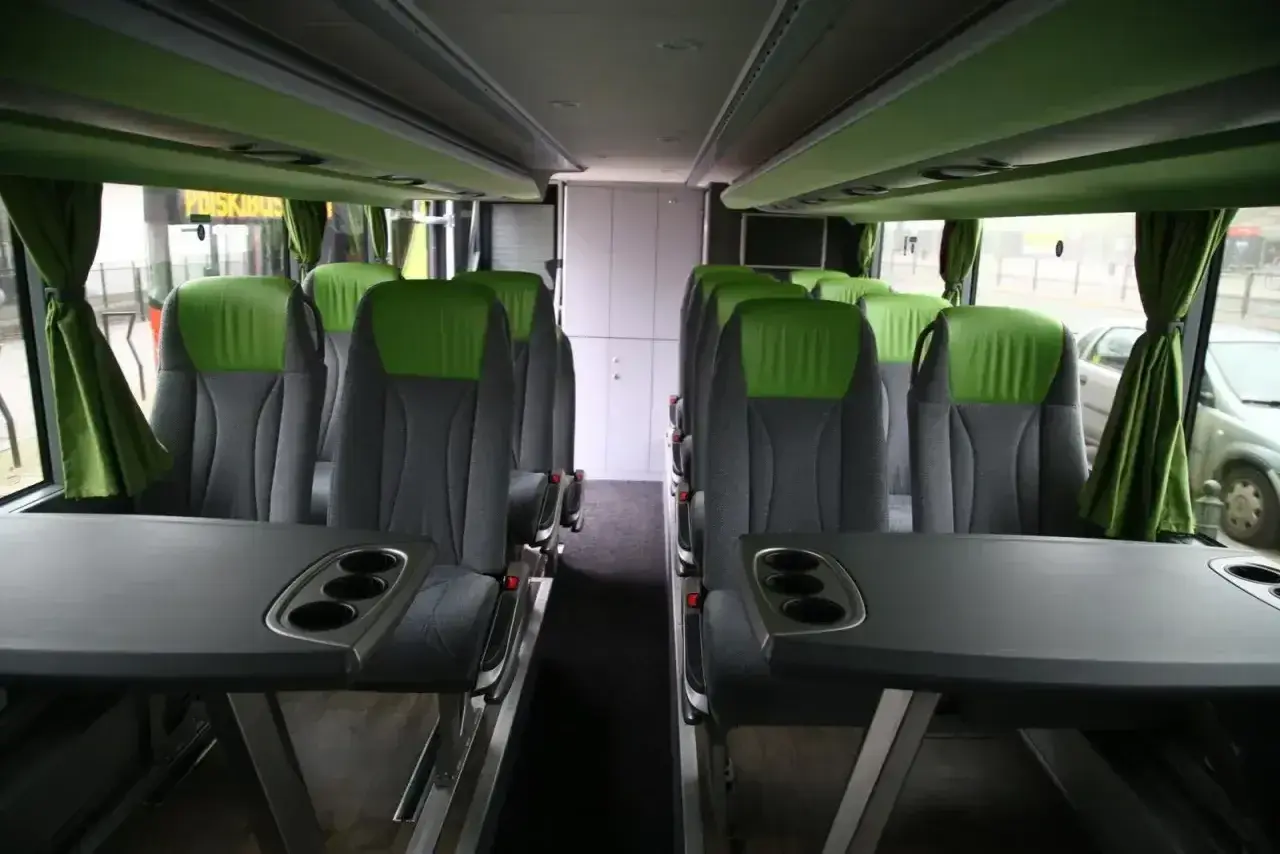 Wygodne, zielono-szare fotele w autobusie FlixBus, z rozkładanymi stolikami i uchwytami na kubki.