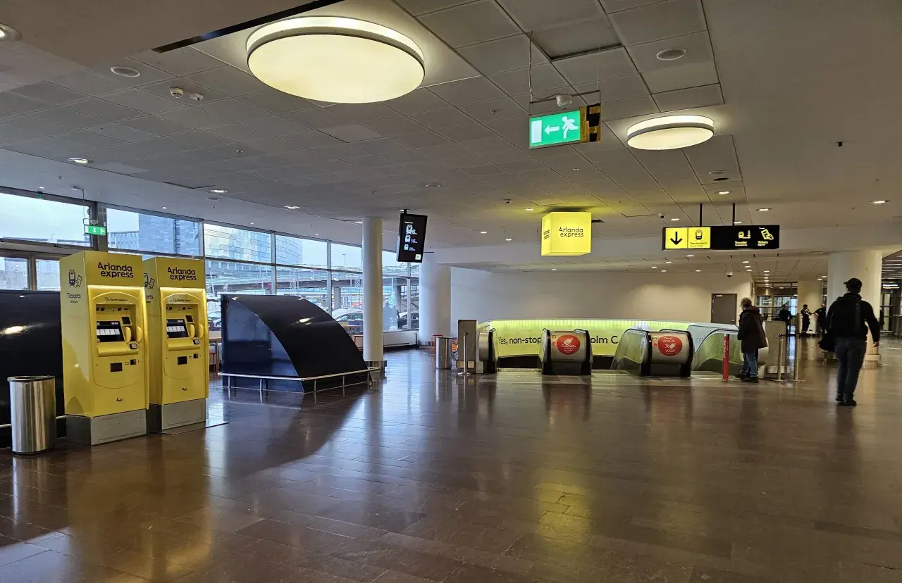 Żółte automaty biletowe Arlanda Express i schody ruchome prowadzące do pociągu.