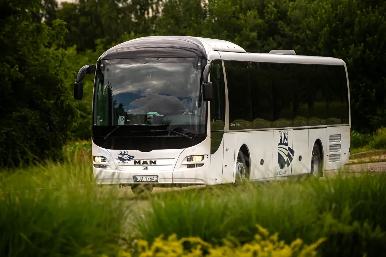 Biały autokar PKS z Jarosławia jedzie przez zielony, bujny krajobraz.