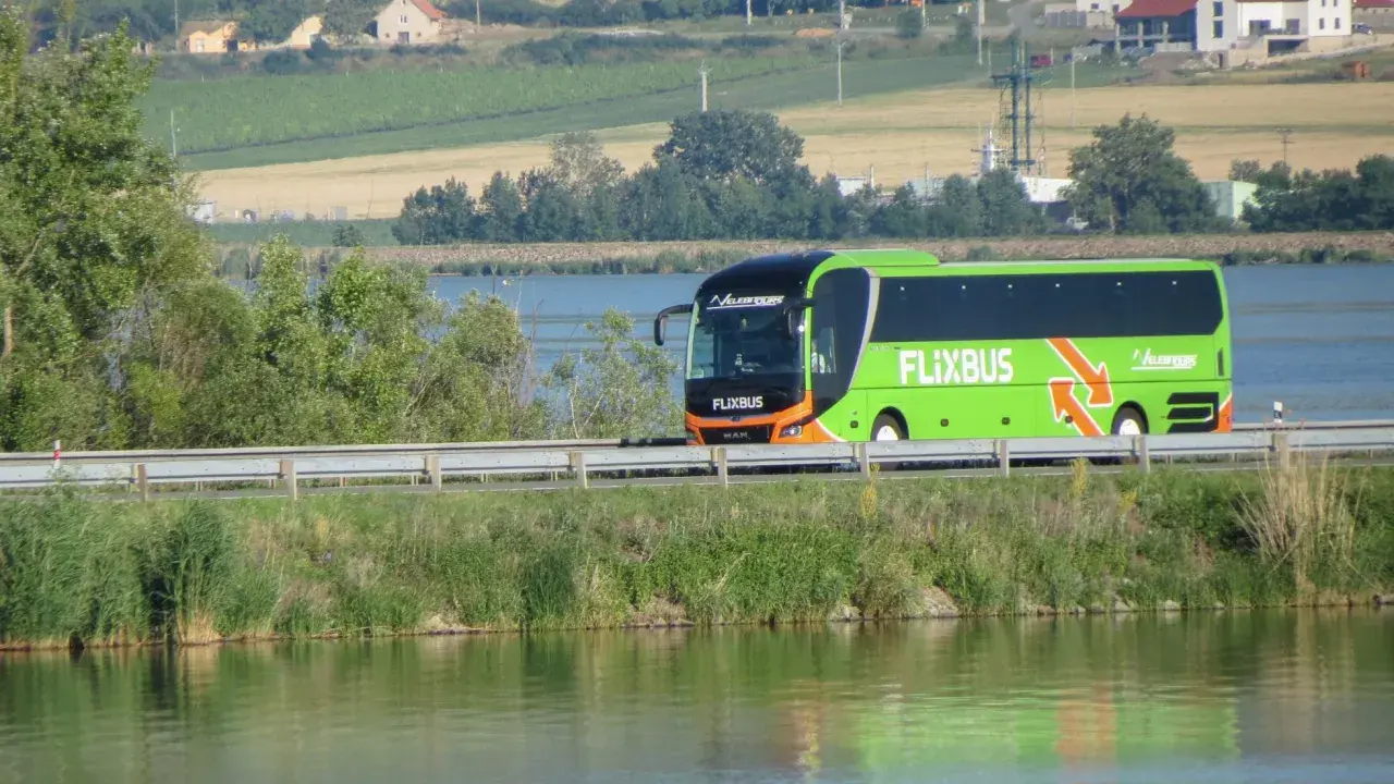 Zielony autobus Flixbus jedzie wzdłuż jeziora. Szukaj flixbus promocje na podróż!