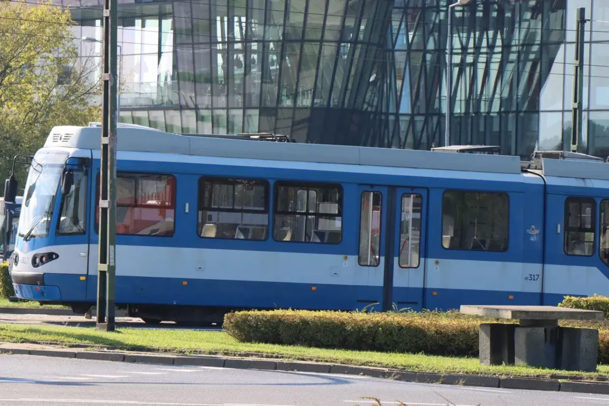 Niebieski tramwaj MPK Kraków stoi na tle nowoczesnego budynku. Sprawdź aktualny mpk kraków bilety cennik przed podróżą.