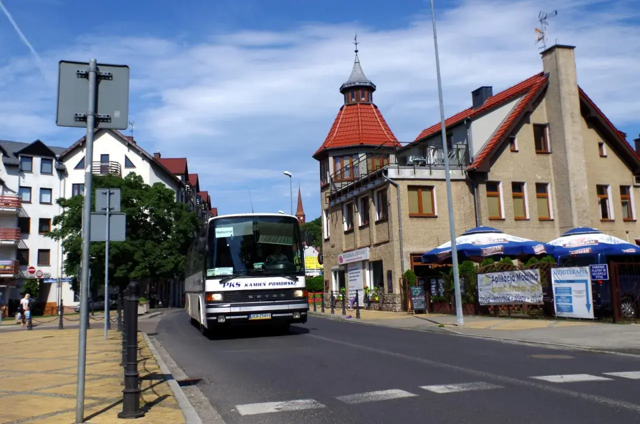 Autobus PKS w Międzyzdrojach zbliża się do dworca kolejowego. Słoneczny dzień, budynki z czerwonymi dachami.