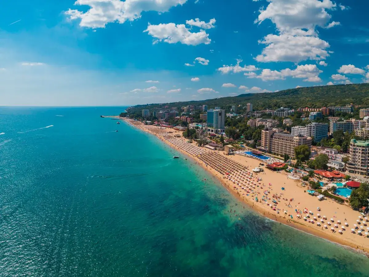 Słoneczna plaża w Złote Piaski, z turkusowym morzem i hotelami w tle. Idealne miejsce na wakacje, niedaleko lotniska.