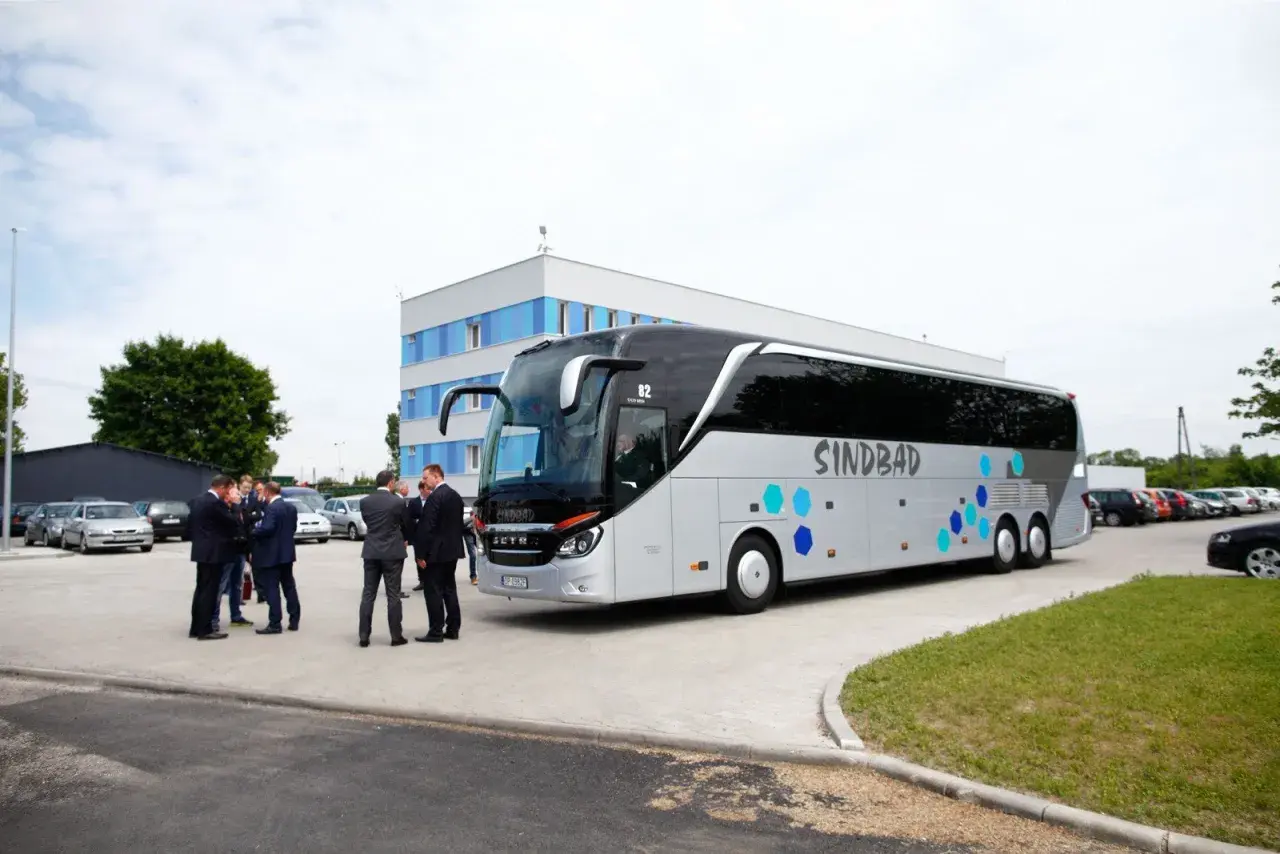 Grupa mężczyzn w garniturach rozmawia przy autokarze Sindbad. Sprawdzają ceny biletów przed podróżą.