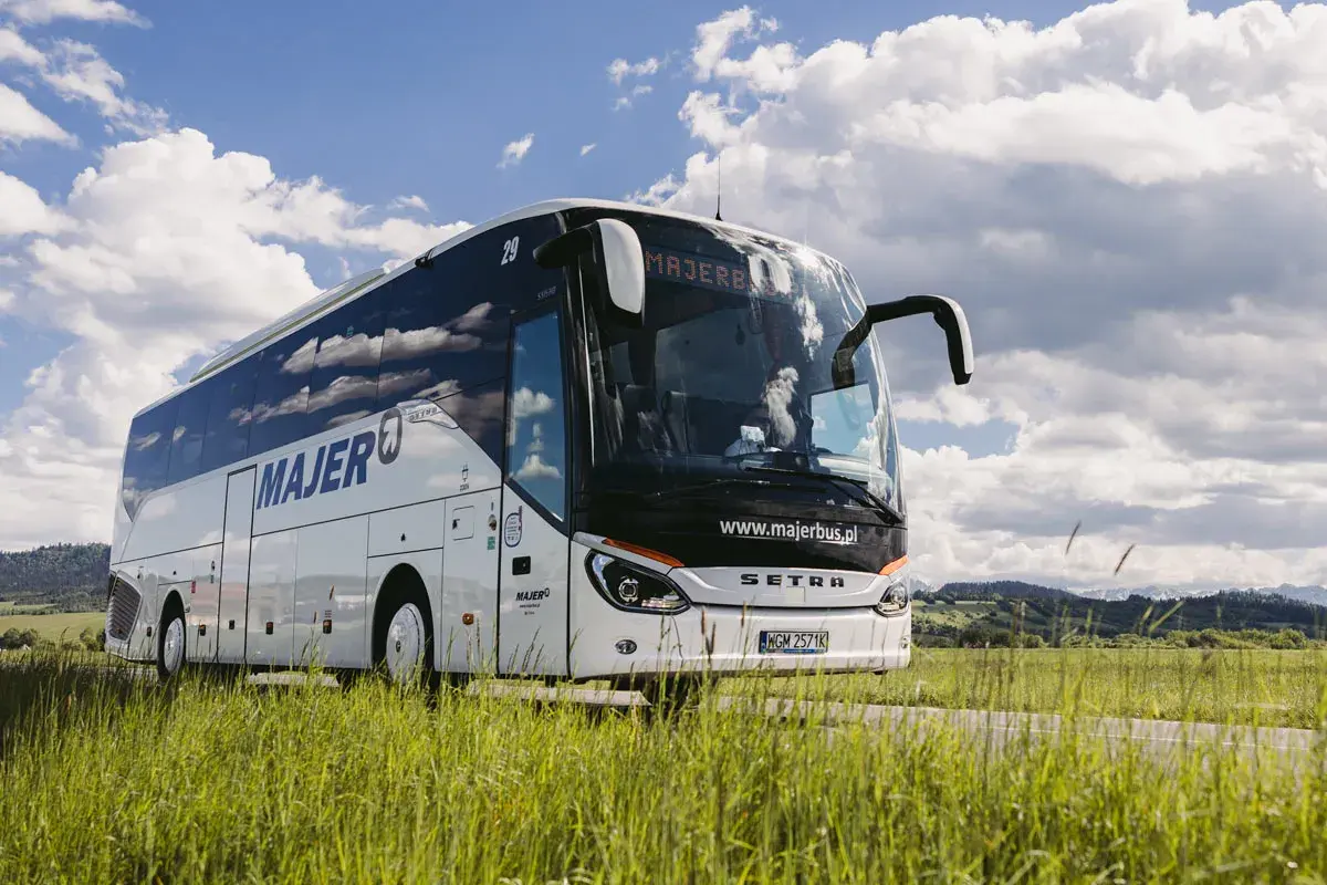 Autobus Majer na trasie Kraków - Mszana Dolna jedzie przez zielone pola pod błękitnym niebem.