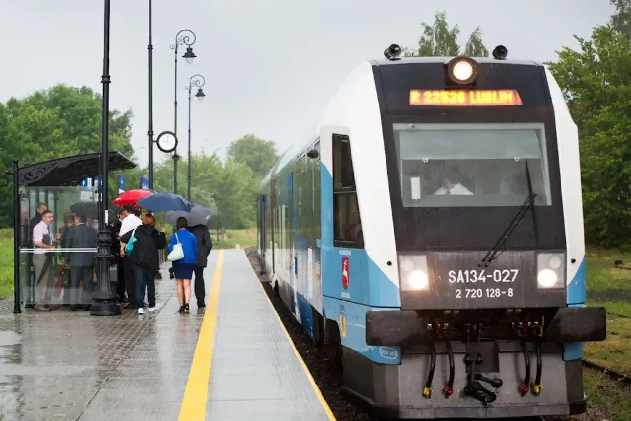 Pasażerowie z parasolami czekają na peronie na pociąg Kolei Lubelskich.