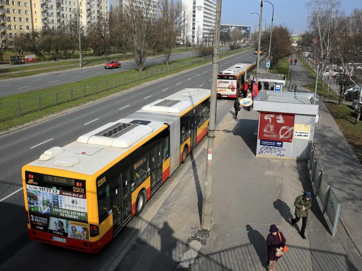 Autobus linii 702 Poznań na przystanku. Zbliża się do zatoczki, gdzie czekają pasażerowie.