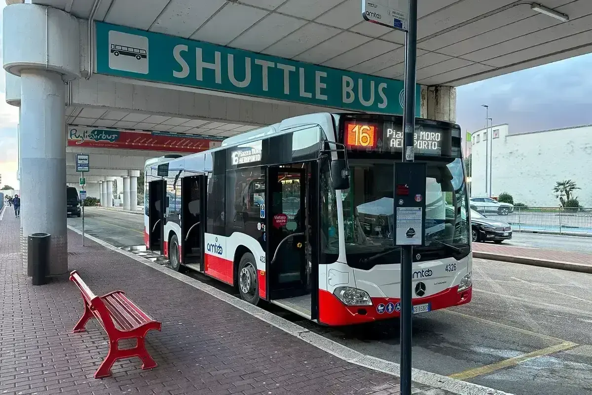 Autobus wahadłowy na lotnisku Bari czeka na pasażerów pod zielonym znakiem "SHUTTLE BUS".