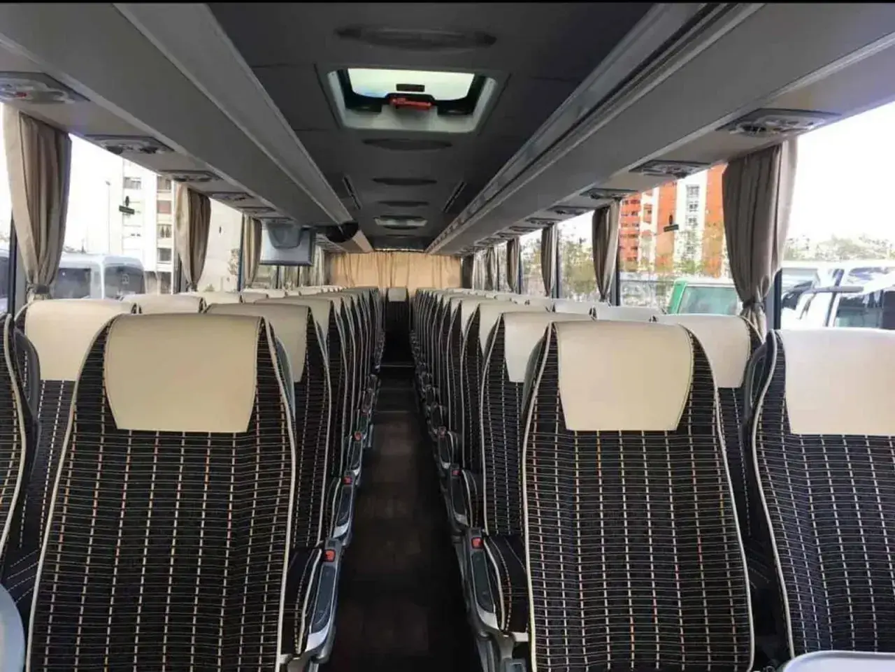 Wnętrze autobusu ze Słowenii, rzędy wygodnych siedzeń z czarno-białą tapicerką i jasnymi zagłówkami.