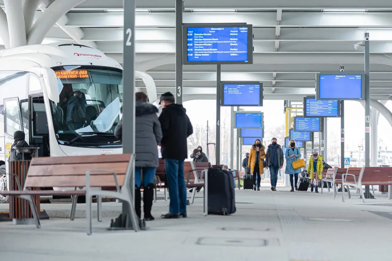 Na dworcu w Katowicach, przy tablicy z odjazdami, ludzie czekają na autobusy. Sprawdź rozkład, by dowiedzieć się, jak dojechać z dworca w Katowicach na Medyków.