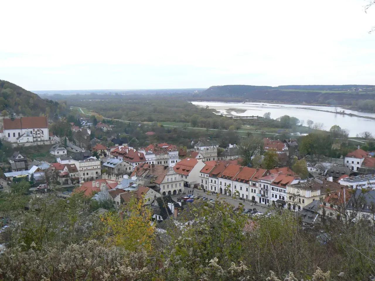 Widok na Kazimierz Dolny z rzeką Wisłą w tle. Planujesz podróż? Sprawdź, jak dojechać do Kazimierza Dolnego pociągiem.