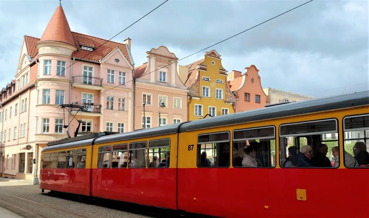 Czerwono-żółty tramwaj z numerem 87 jedzie ulicą Grudziądza. W tle kolorowe kamienice.