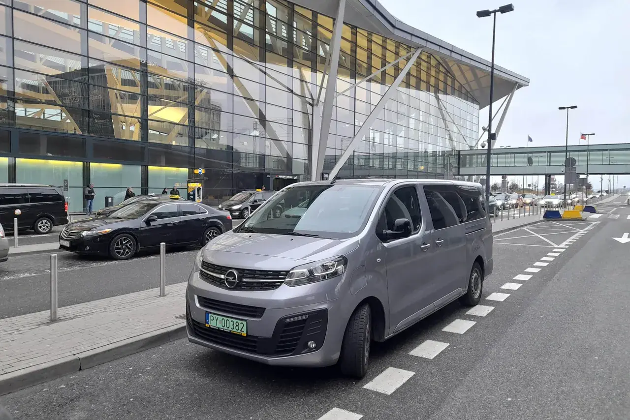 Srebrny bus czeka na pasażerów przed nowoczesnym terminalem lotniska. Może to być transport z Koszalina do Gdańska na lotnisko.
