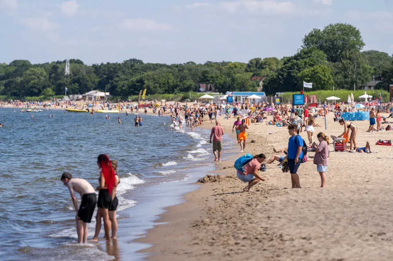 Ludzie cieszą się słońcem i morzem na plaży. W tle widać las. Idealne miejsce na podróż pociągiem nad morze z Poznania.