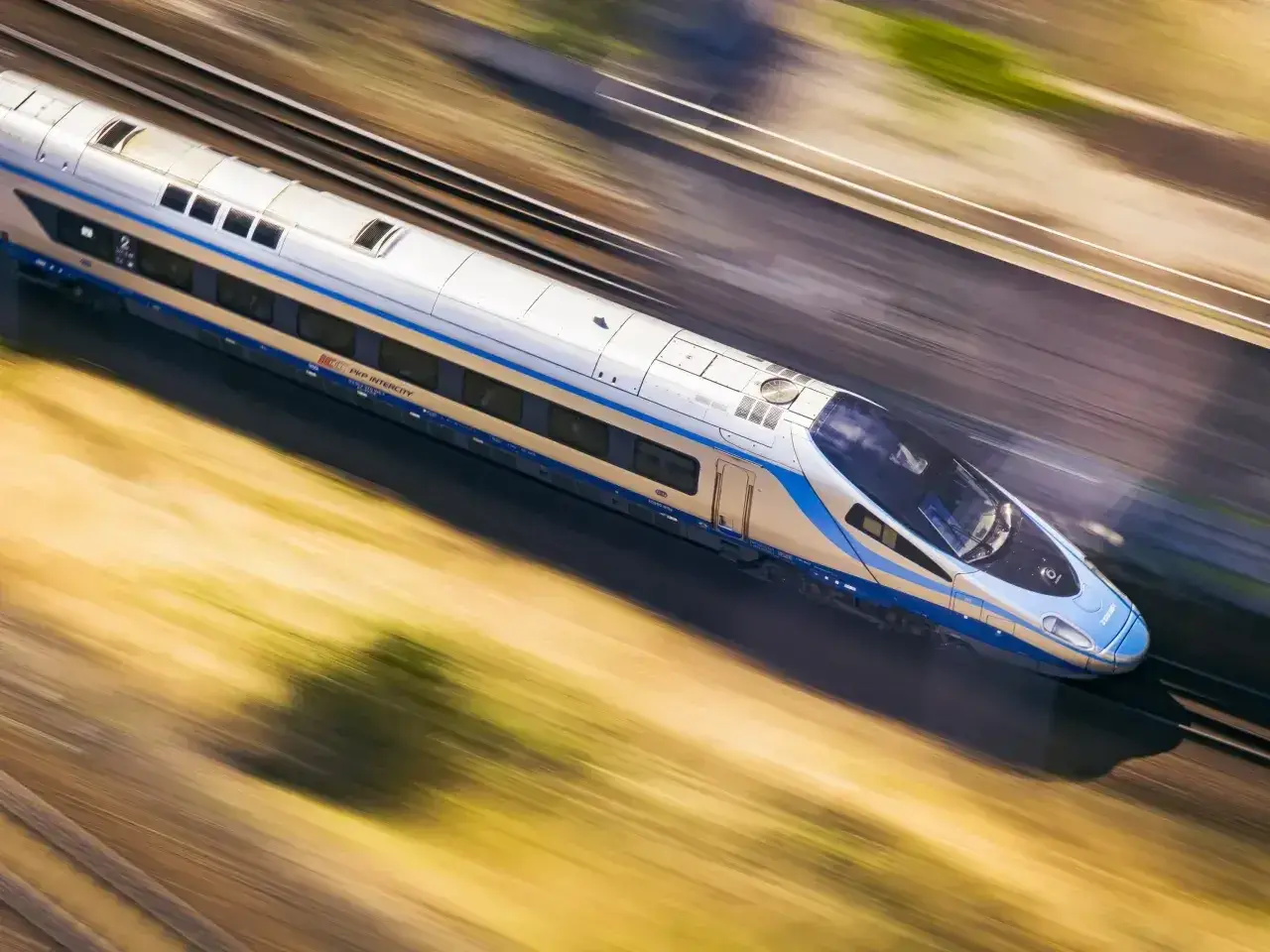 Pociąg PKP Intercity pędzi z ogromną prędkością, rozmazując krajobraz.