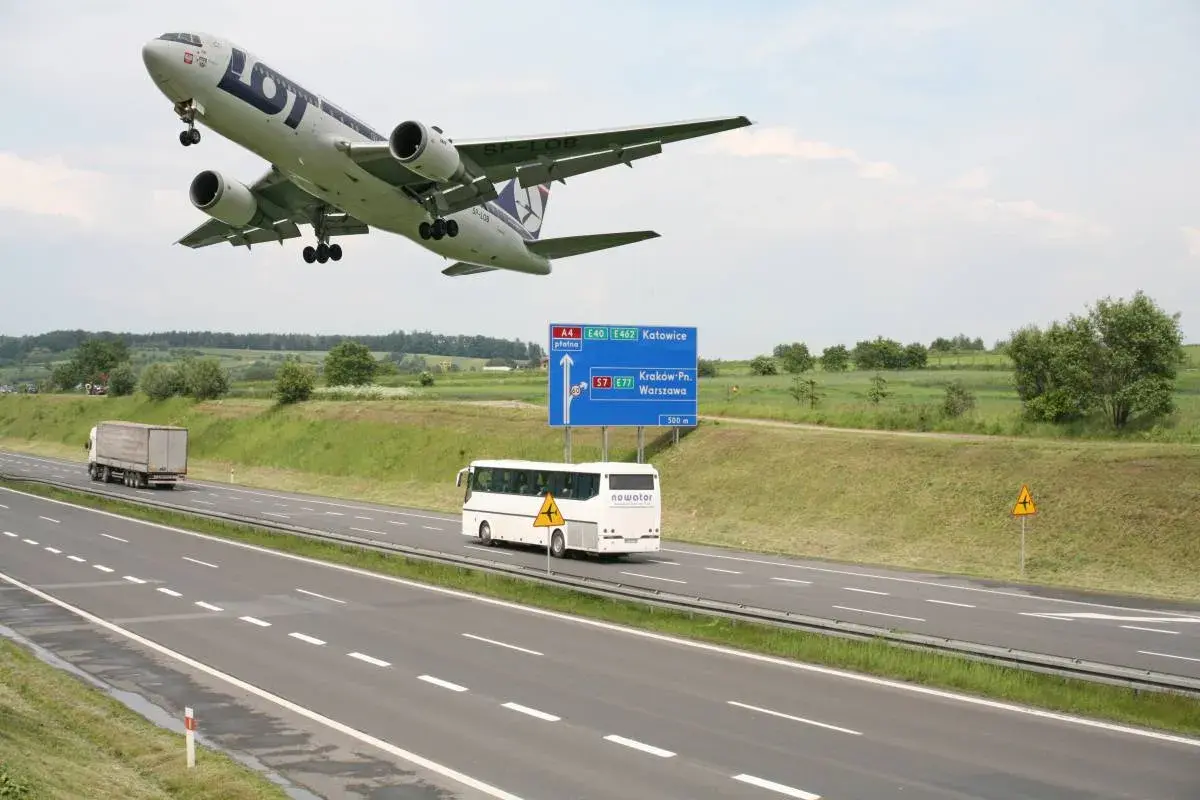 Samolot LOT leci nisko nad autostradą A4 w kierunku Katowic. Obok jedzie autobus, a w oddali widać drogę do Krakowa i Warszawy.