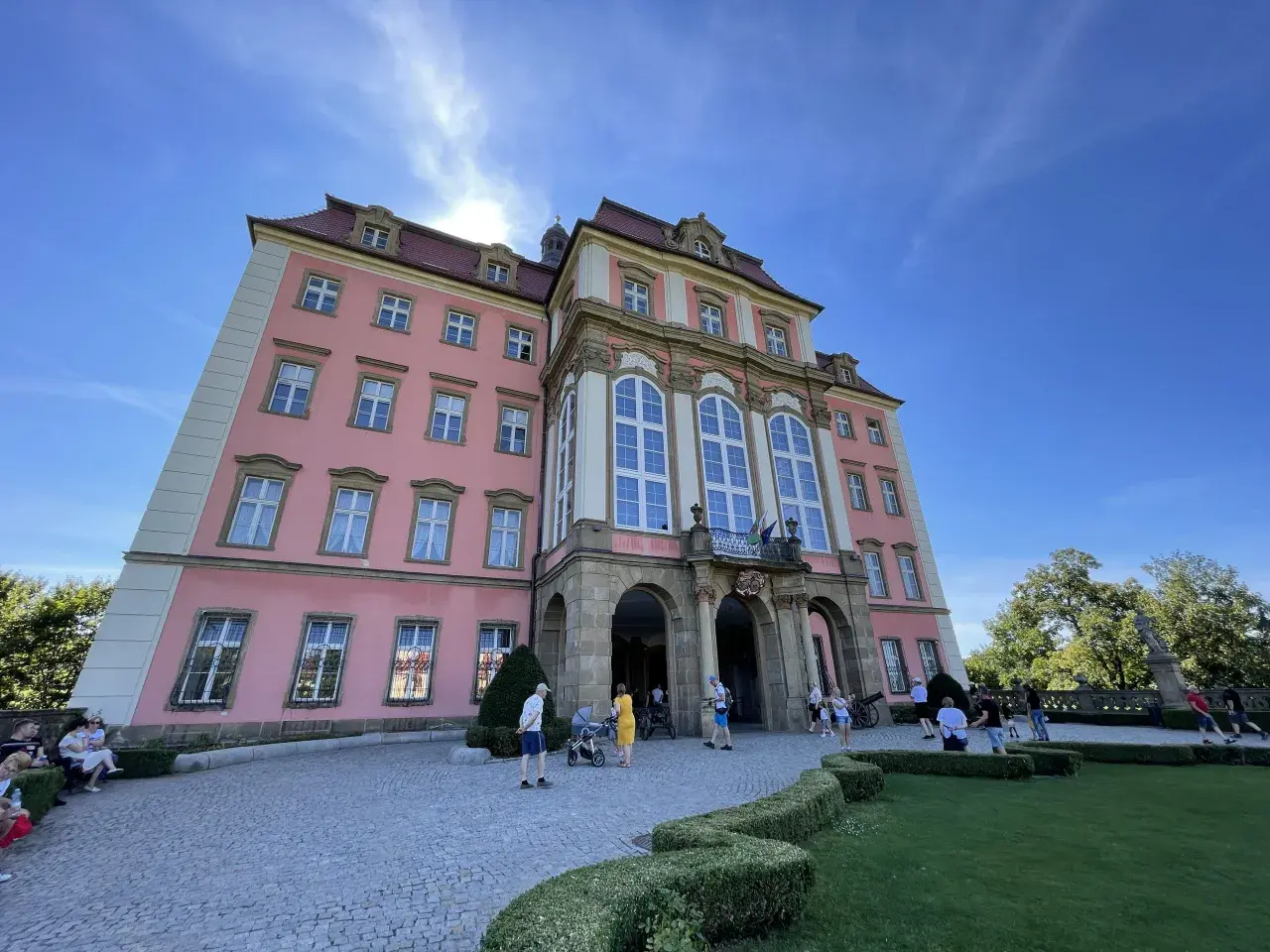 Zamek Książ, łatwy dojazd PKP, zachwyca różową fasadą i barokową architekturą. Turyści spacerują po brukowanym dziedzińcu.