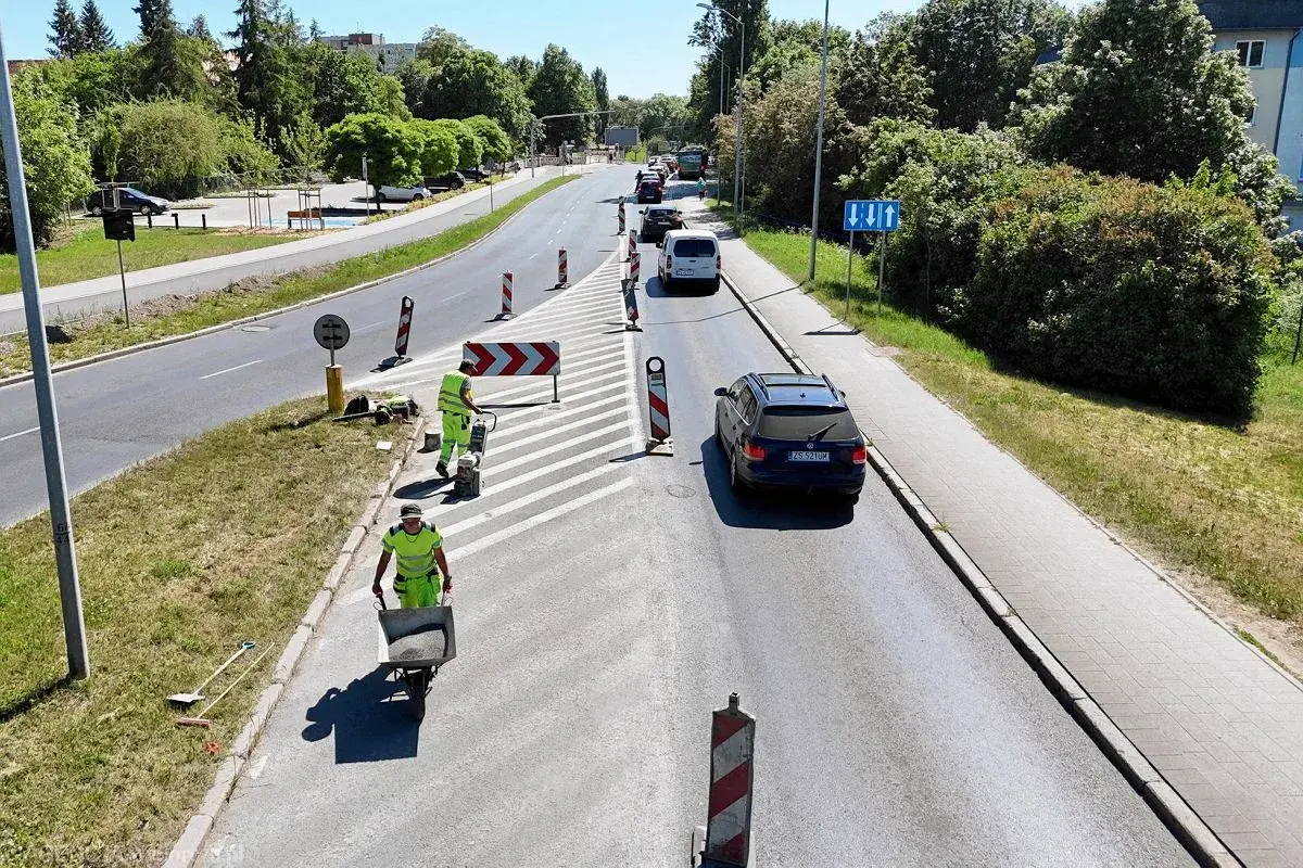 Prace drogowe na linii 101 Szczecin. Robotnicy w kamizelkach odblaskowych przygotowują nawierzchnię, jeden z nich pcha taczkę z materiałem.