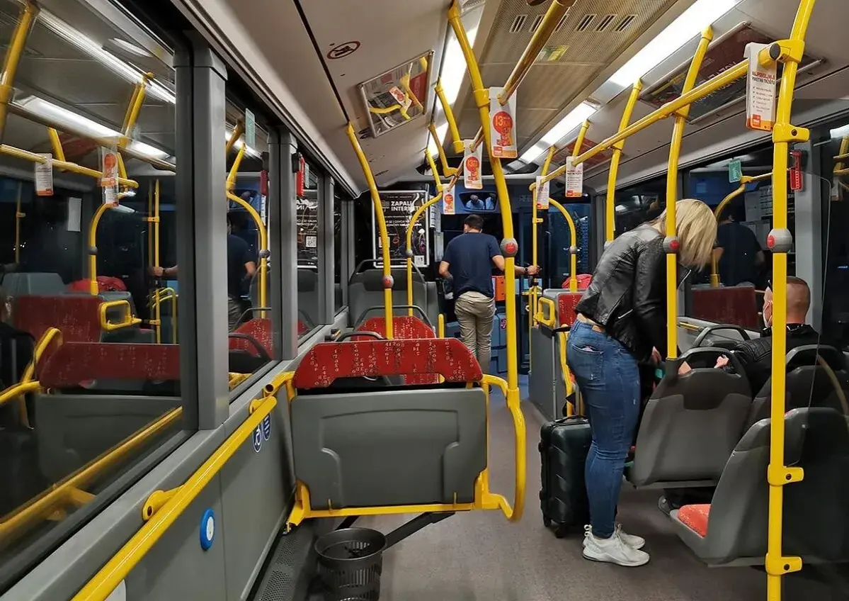 Wnętrze autobusu, żółte poręcze, siedzenia, pasażerowie z bagażem. Zadar komunikacja miejska.