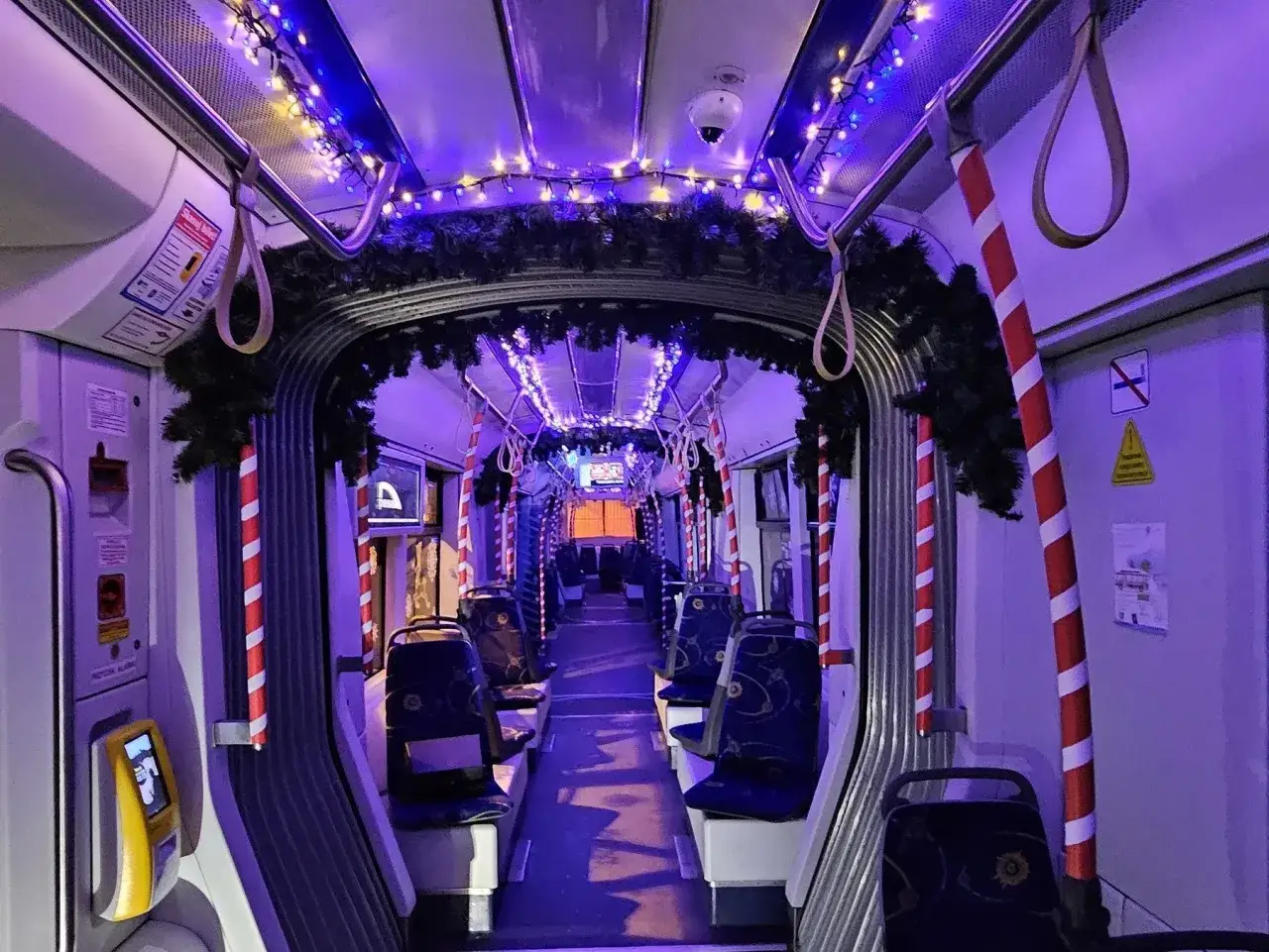 Wnętrze świątecznego tramwaju w Warszawie, ozdobionego lampkami i gałązkami choinki.