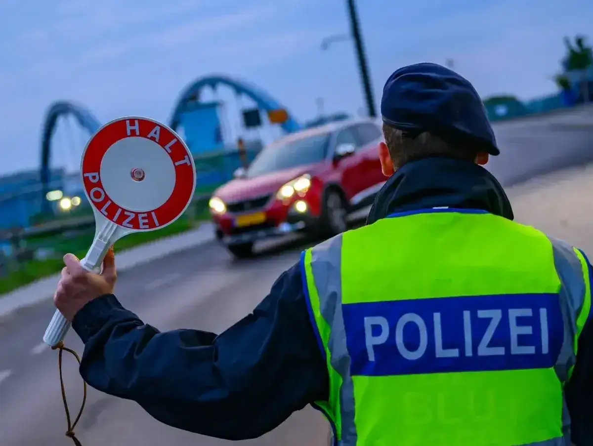 Policjant zatrzymuje czerwony samochód, trzymając znak 