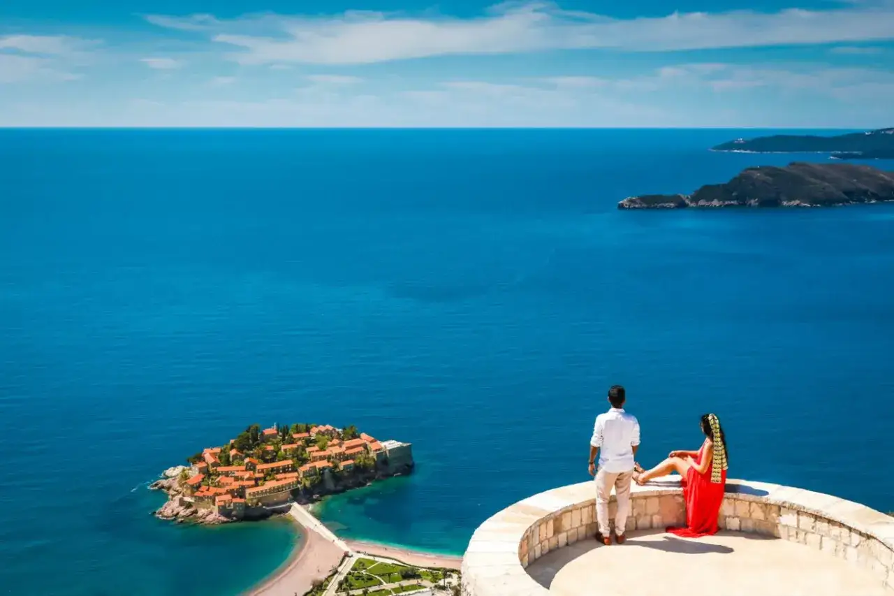 Para zapatrzona w widok na wyspę Sveti Stefan, marząca o podróży do Budvy. Lotnisko w pobliżu to idealny punkt startowy.