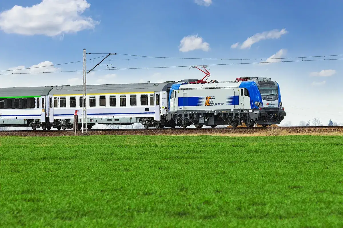 Pociąg PKP Intercity z nowoczesną lokomotywą mknie przez zielone pola. Idealny na weekendową podróż z biletem weekendowym PKP.