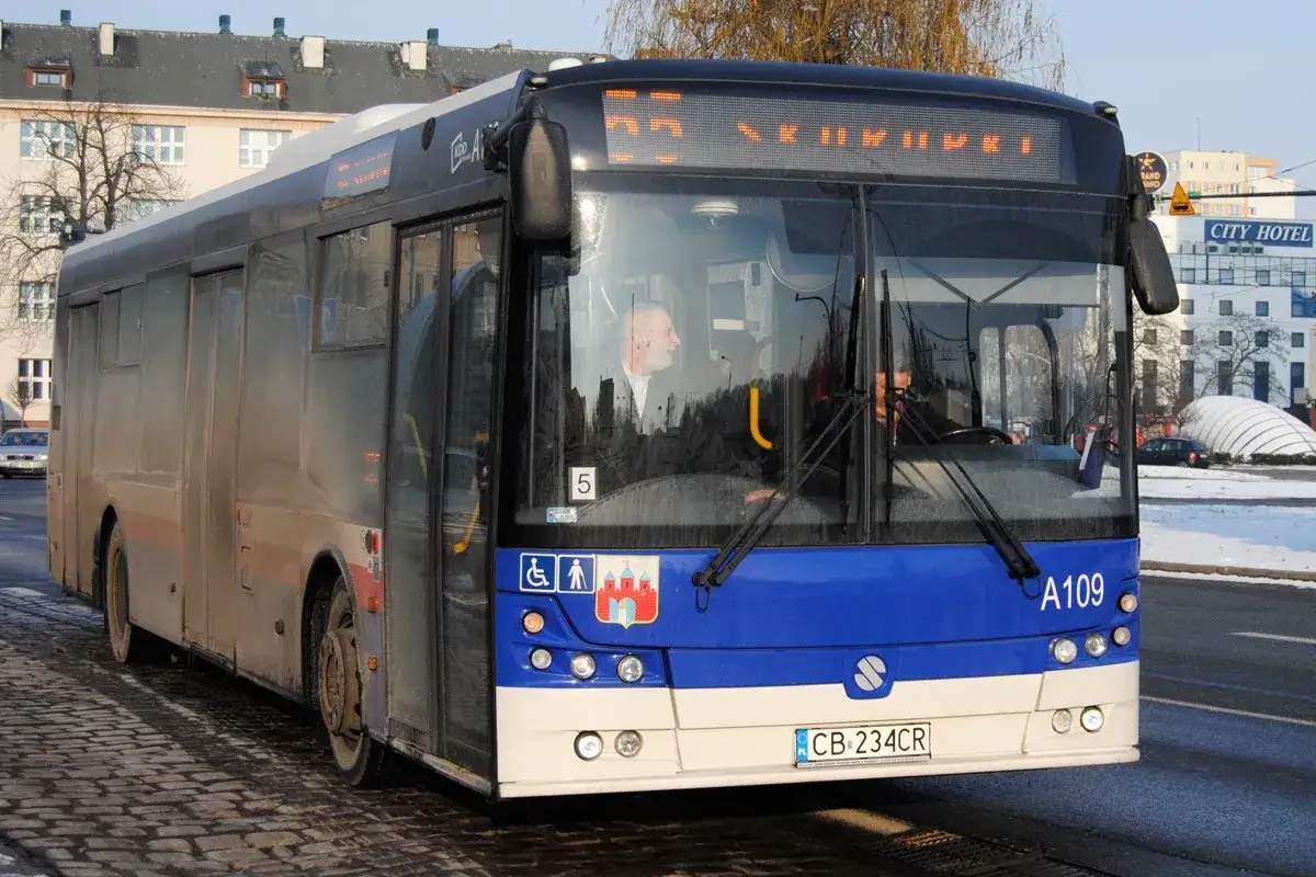 Autobus 55 Bydgoszcz z kierowcą za kierownicą, jadący po brukowanej ulicy.