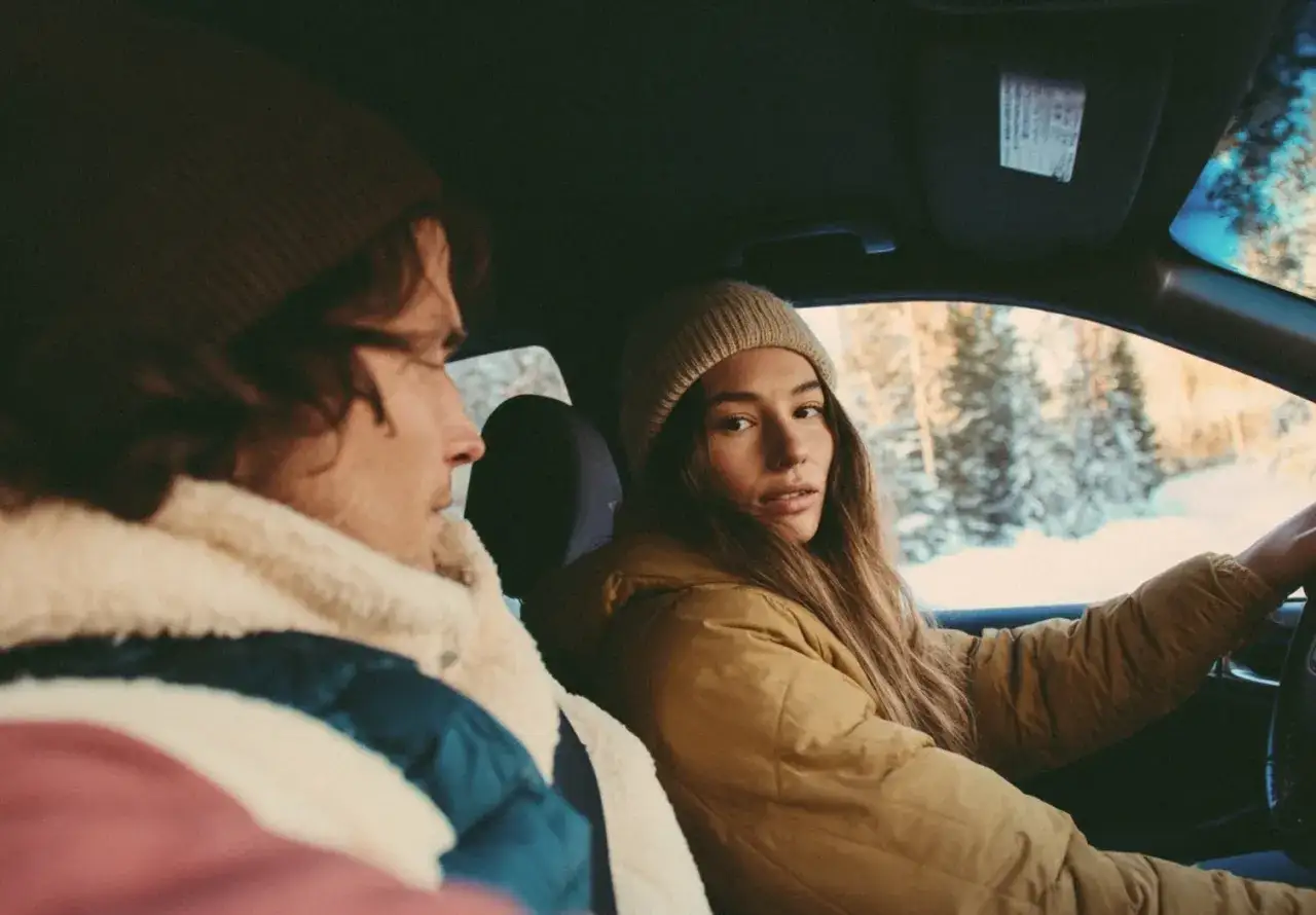 Para młodych w zimowych kurtkach i czapkach podczas carpoolingu w zaśnieżonym lesie.