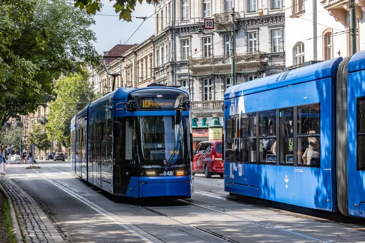 Dwa niebieskie tramwaje na ulicy w Krakowie. Komunikacja miejska w pełnym ruchu, z zabytkową kamienicą w tle.