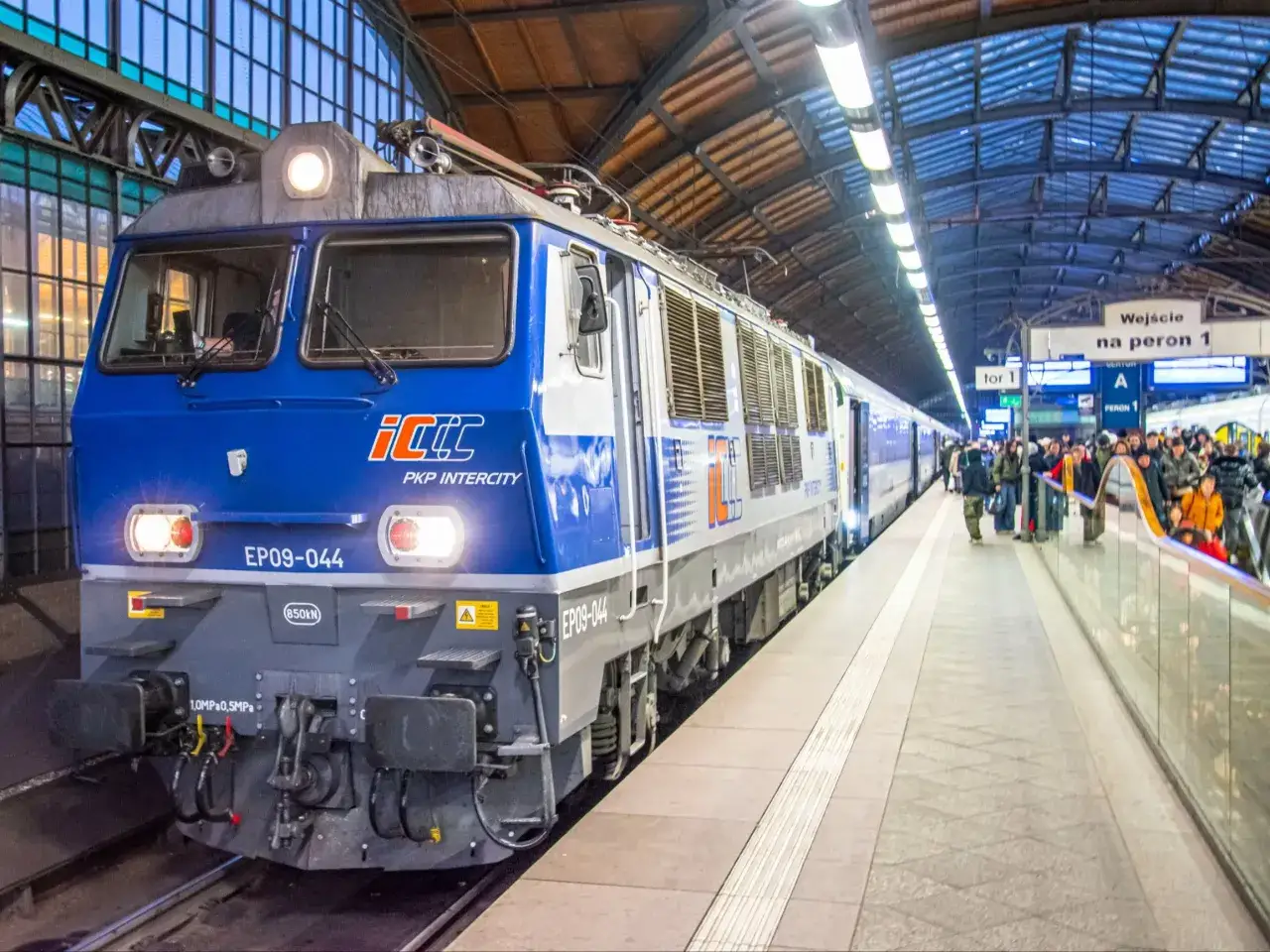 Niebieski pociąg Intercity EP09-044 na peronie. Pasażerowie czekają na podróż, zastanawiając się, z jaką prędkością jedzie pociąg Intercity.