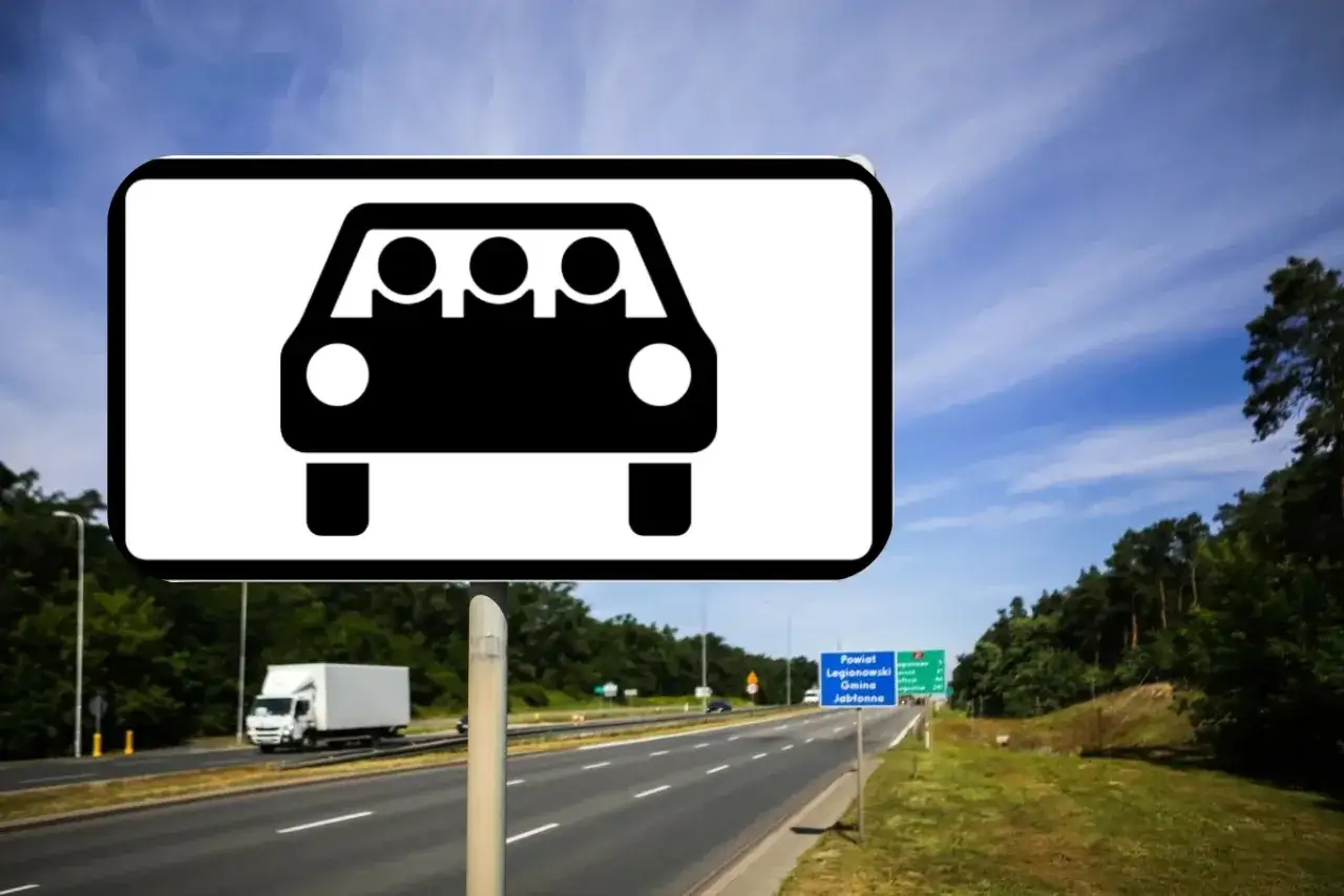 Znak informuje o carpoolingu, czyli wspólnym dojeździe do pracy. Na drodze widać samochody i drzewa.