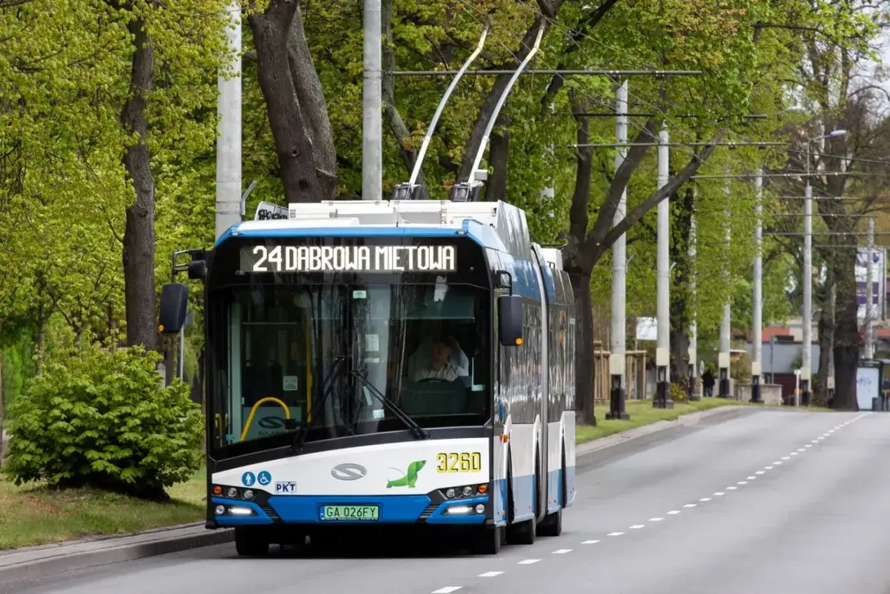 Trolejbus linii 24 jedzie ulicą w Gdyni, otoczony zielenią.