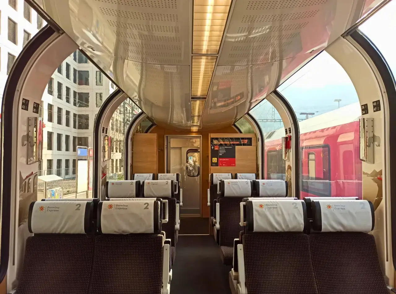 Wnętrze wagonu Bernina Express z wygodnymi siedzeniami i panoramicznymi oknami. Bilety na tę podróż to gwarancja niezapomnianych widoków.