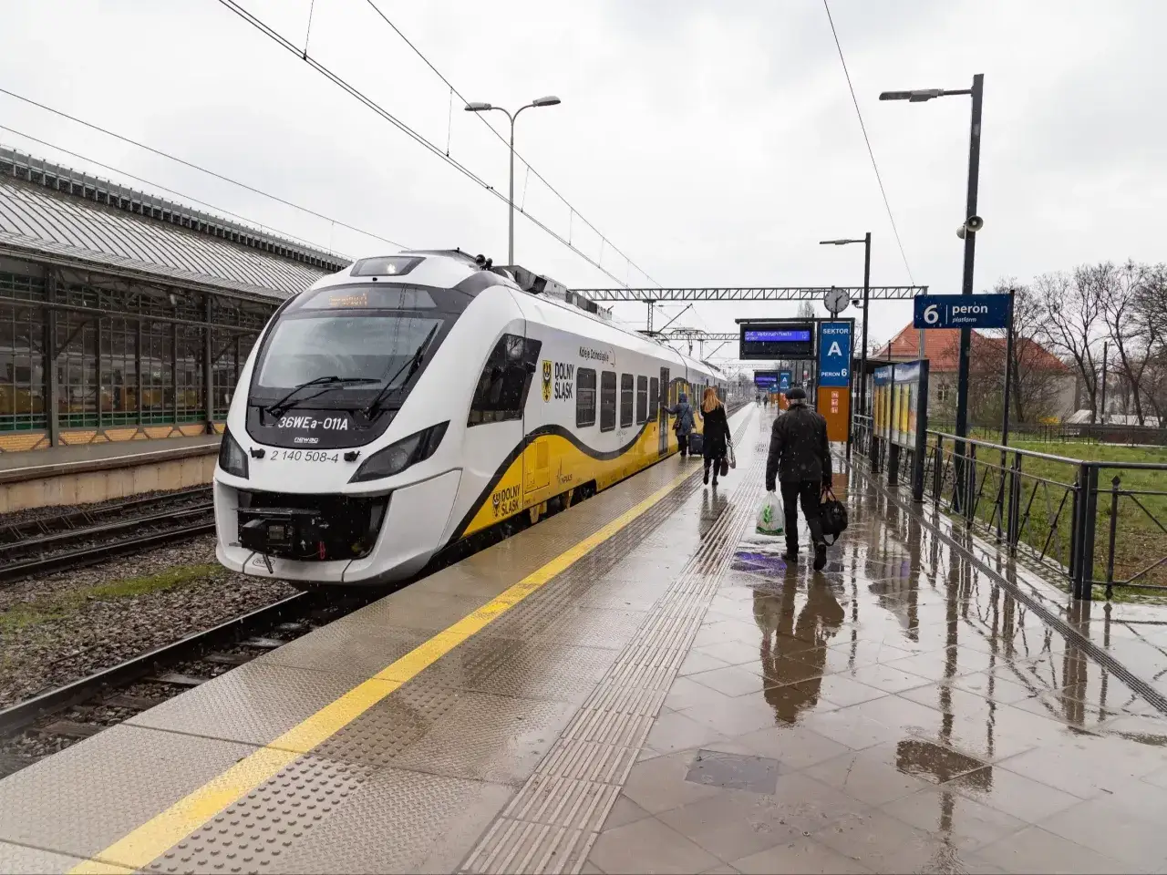 Pasażerowie wsiadają do pociągu, a obok stoi hulajnoga elektryczna.