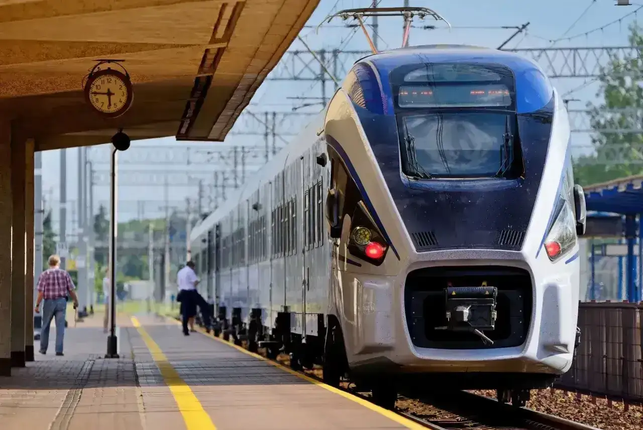 Na dworcu stoi nowoczesny pociąg Intercity. Zegar nad peronem pokazuje, czy można jechać wcześniejszym pociągiem Intercity.