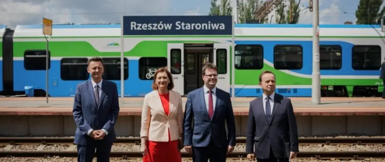 Cztery osoby stoją na peronie przed pociągiem z napisem 