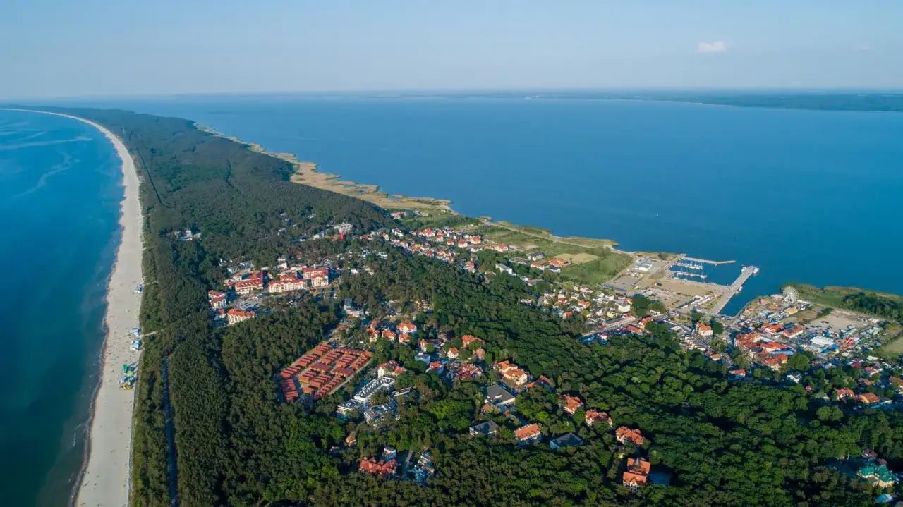 Widok na Krynicę Morską z lotu ptaka. Widać plażę, morze, zalew, las i zabudowania. Wyobraź sobie, że do tego malowniczego miejsca dojeżdża pociąg.