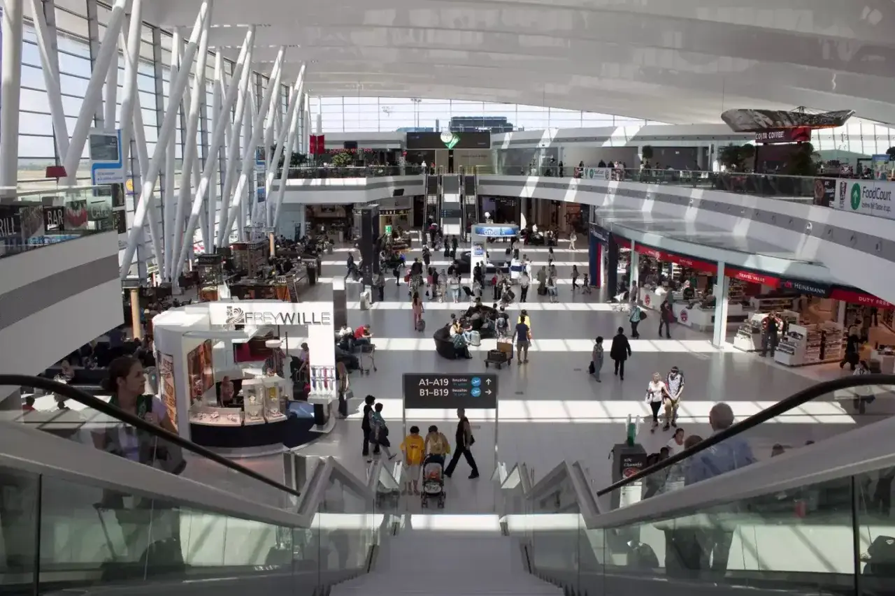 Tętniący życiem terminal lotniska w Budapeszcie. Ludzie poruszają się po jasnej, przestronnej hali, szukając transportu z lotniska, sklepów i kawiarni.