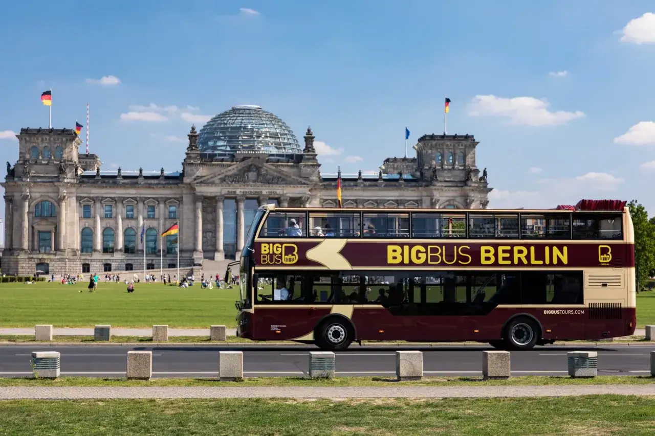 Dwupiętrowe autobusy Big Bus Berlin przejeżdżają obok Reichstagu w słoneczny dzień.
