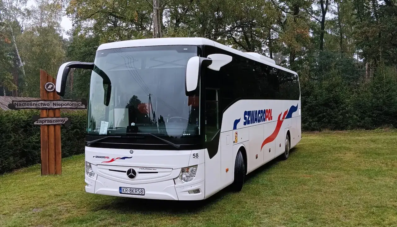 Biały autokar Szwagropol, idealny na podróż z Nowego Sącza do Krakowa, zaparkowany przy leśnym drogowskazie.
