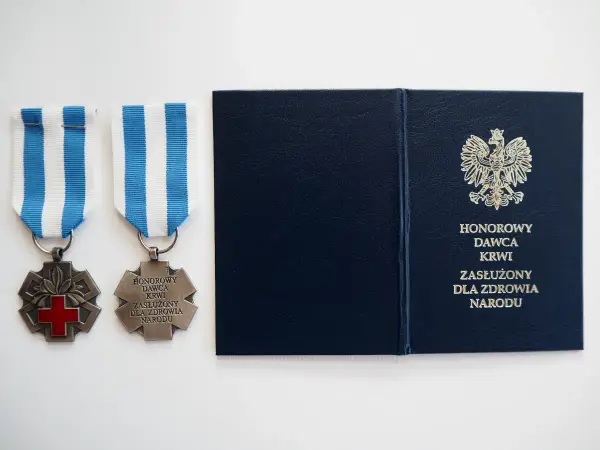 Dwa medale z czerwonym krzyżem i napisem "Honorowy Dawca Krwi Zasłużony dla Zdrowia Narodu" oraz granatowa teczka z godłem Polski.